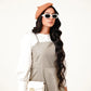 A woman wearing a beige pinafore dress with a white top, featuring a vintage-inspired neckline and wide straps.